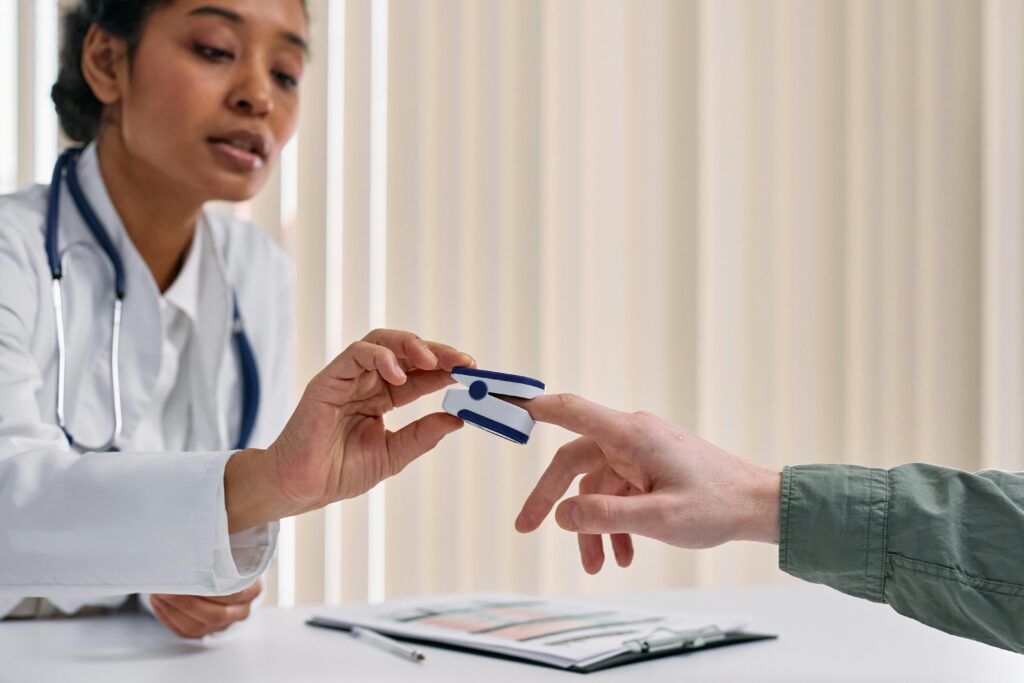 Healthcare worker checking patient vitals with a pulse oximeter in a clinical setting.